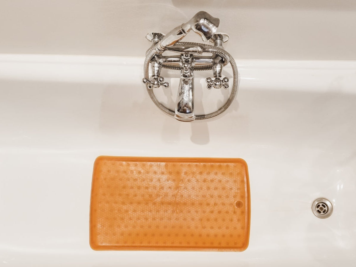 White bathtub with an orange bath mat and decorative elements in a bathroom setting.
