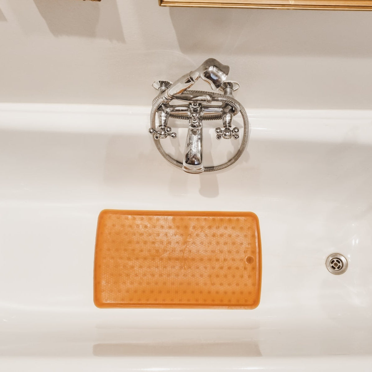 White bathtub with an orange bath mat and decorative elements in a bathroom setting.