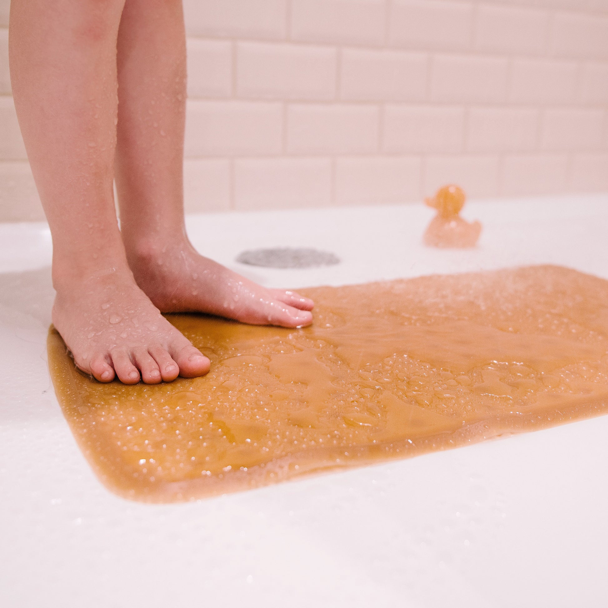 Child's feet on Honeycomb Anti Slip Baby Bath Mat in a bath, showcasing the mat's natural rubber and anti-slip features.