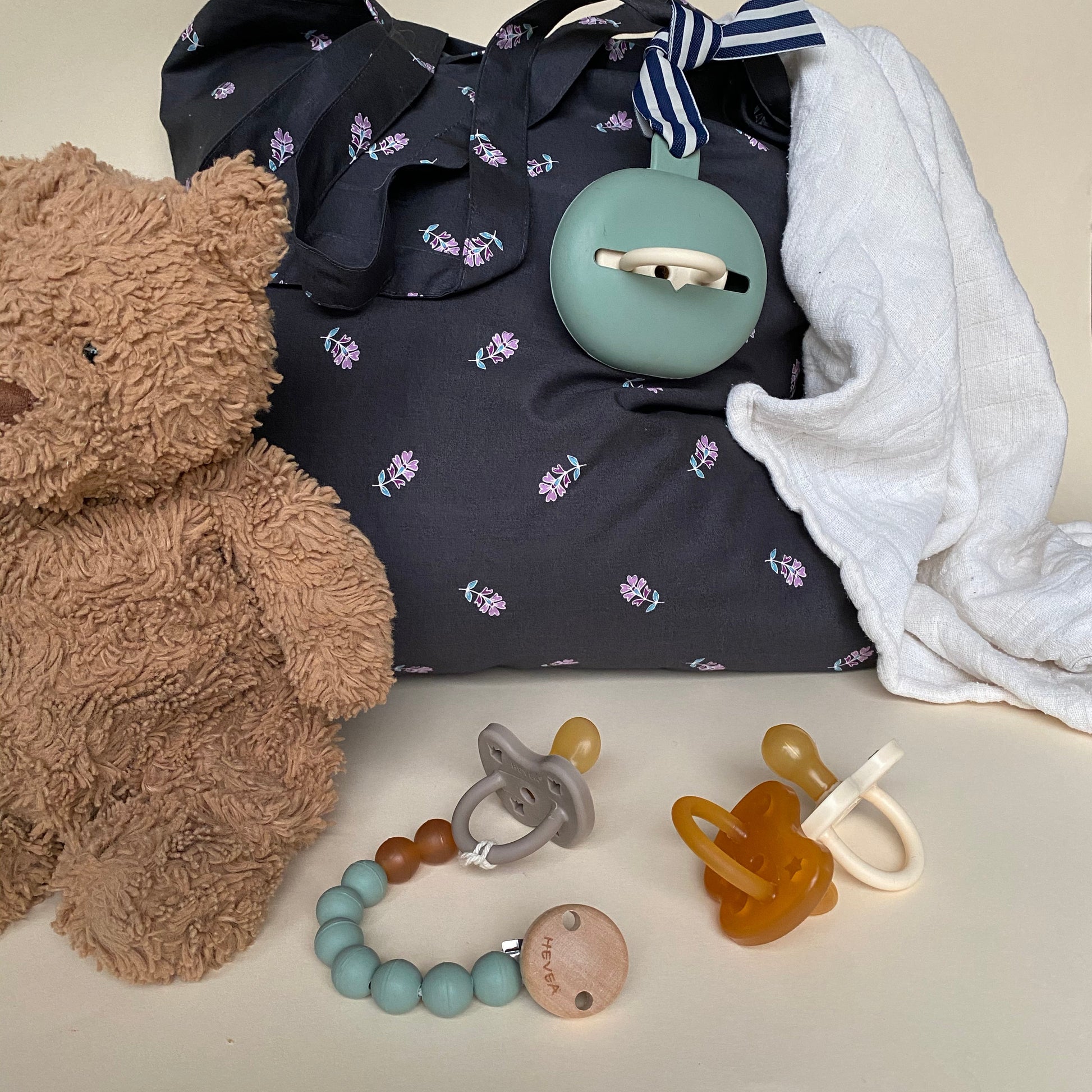 Baby items including a teddy bear, pacifiers, and a teething ring on a neutral background