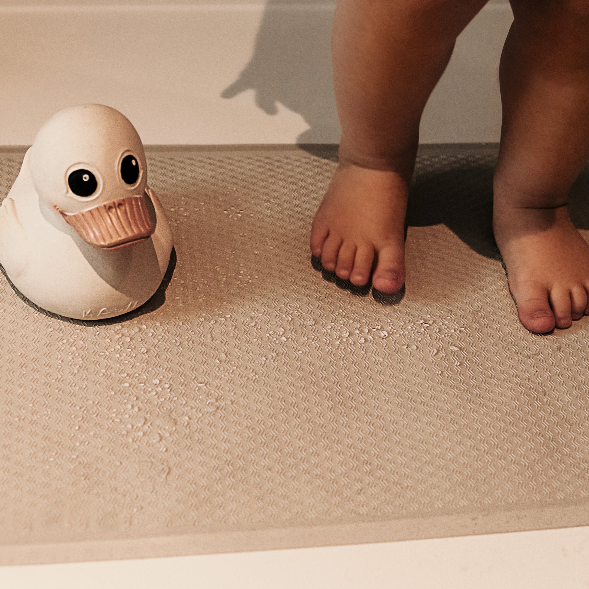 White duck-shaped bath toy on a bathtub floor with a child's feet in the background