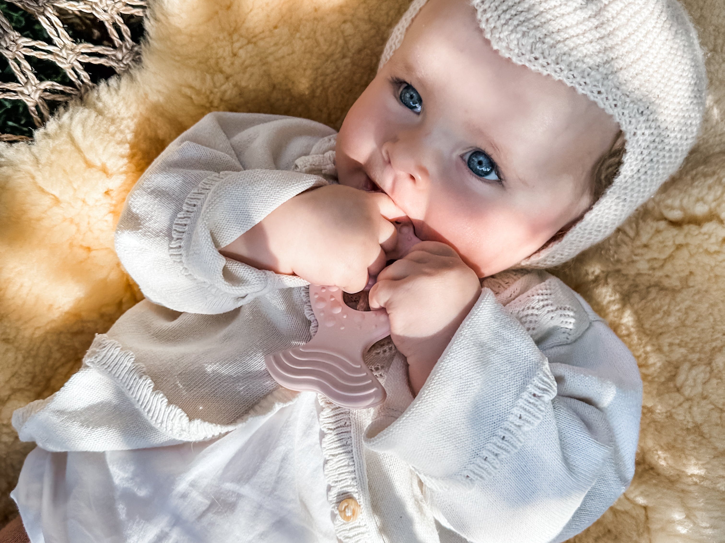 Baby wearing a white outfit and knit hat lying on a textured surface