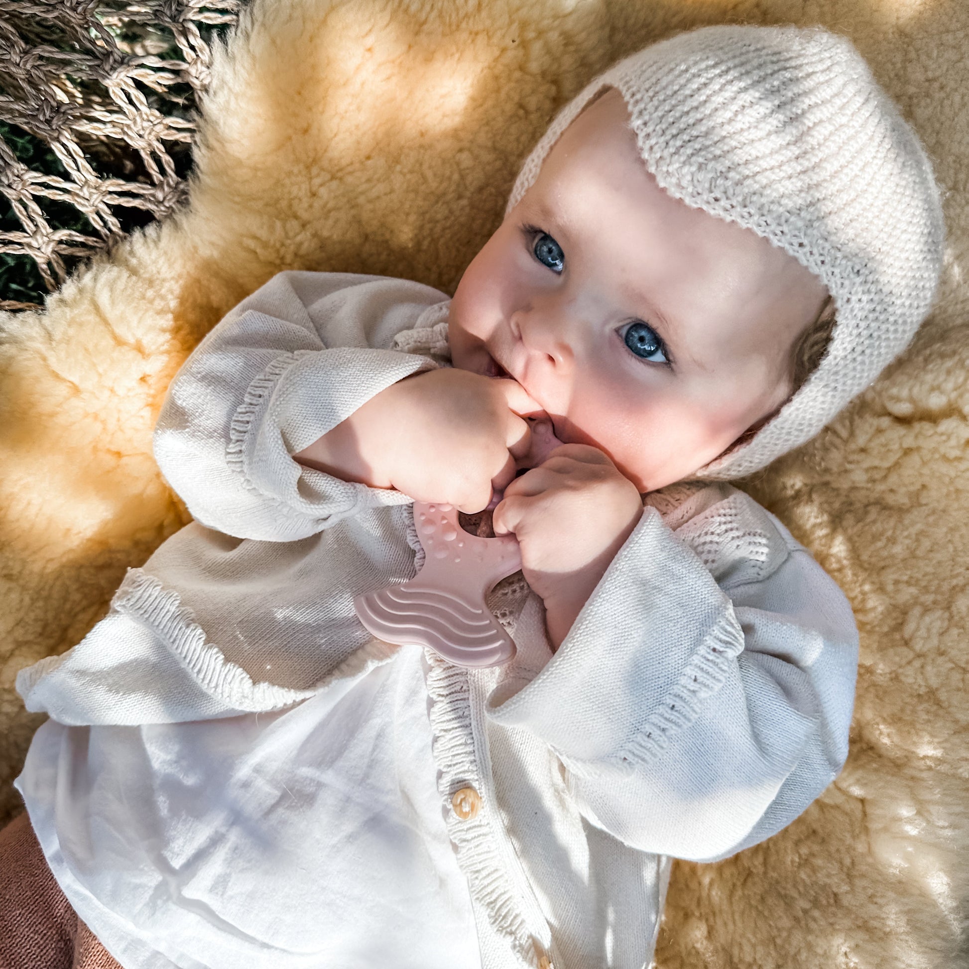 Baby wearing a white outfit and knit hat lying on a textured surface