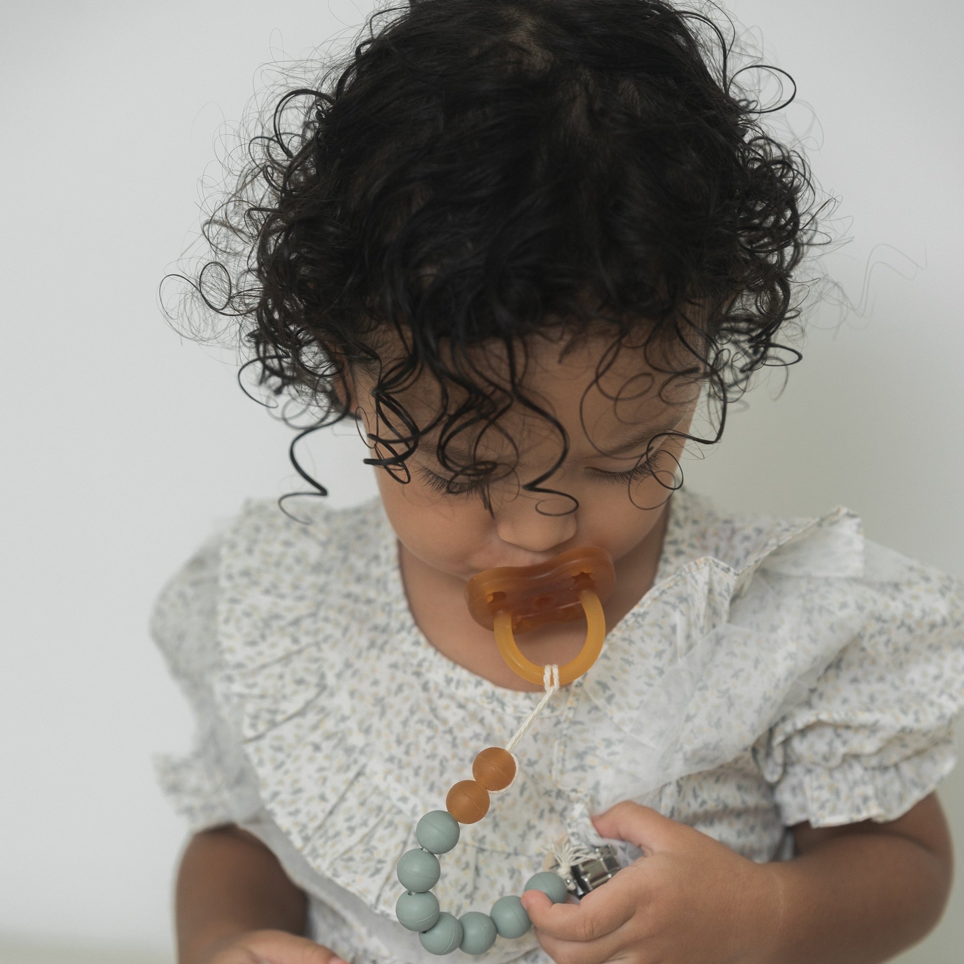 Child wearing a pacifier and holding a toy with a plain background